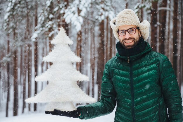 Mann in der Pelzmütze mit den Ohrenklappen, die einen Baum halten