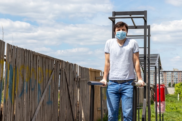 Mann in der schützenden blauen medizinischen Maske, die einen Barstand auf dem Außensportplatz tut