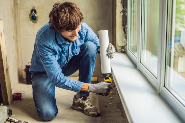 Mann in einem blauen Hemd macht Fensterinstallation. Verwendung eines Montageschaums