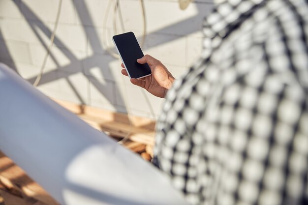 Mann in einem karierten Hemd mit seinem Smartphone und mit Papier