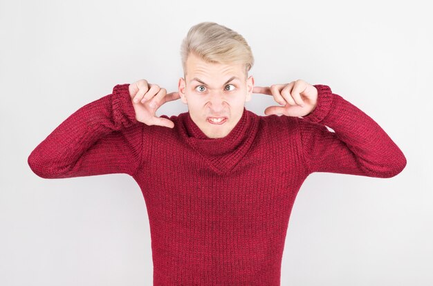 Mann in einem roten Heimpullover stecken seine Ohren mit den Fingern gegen das laute Geräusch.