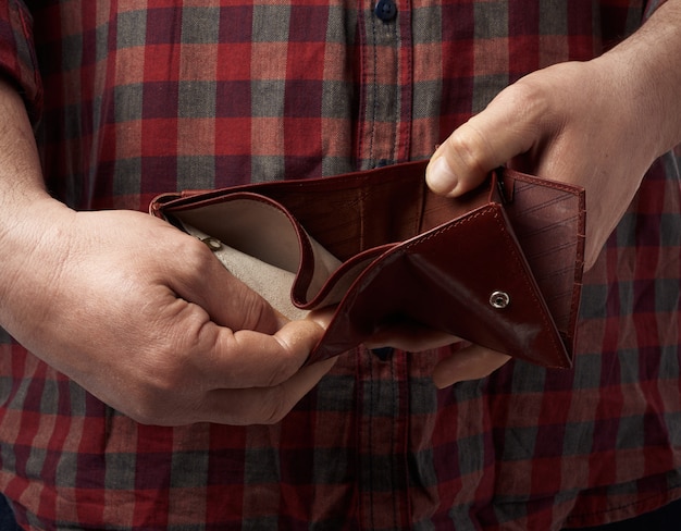 Mann in einem roten karierten Hemd hält eine leere braune Lederbrieftasche