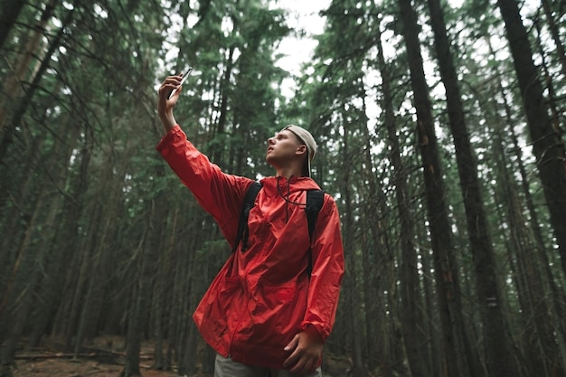 Mann in einem roten Regenmantel steht in einem dichten Nadelwald auf einer Wanderung und fängt einen Anruf auf