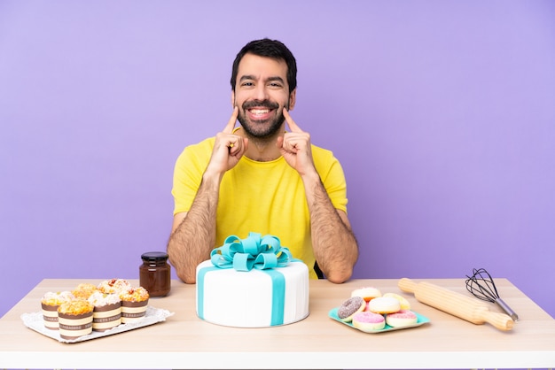 Mann in einem Tisch mit einem großen Kuchen, der mit einem glücklichen und angenehmen Ausdruck lächelt