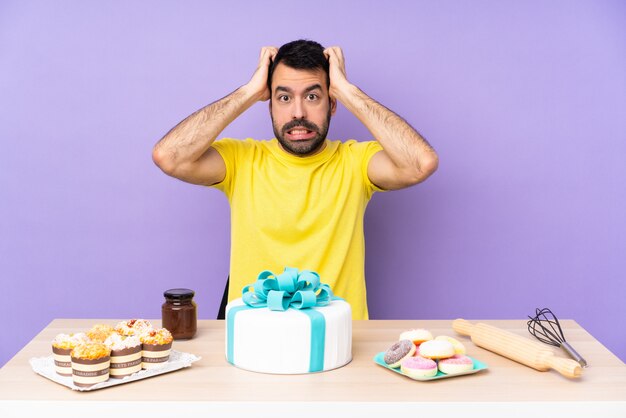 Mann in einem Tisch mit einem großen Kuchen frustriert und nimmt Hände auf den Kopf