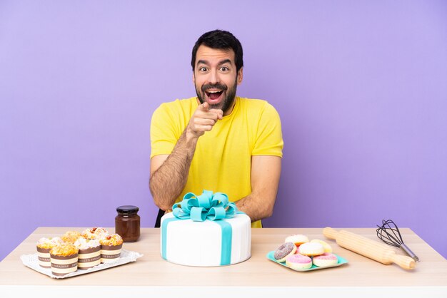 Mann in einem Tisch mit einem großen Kuchen überrascht und nach vorne zeigend