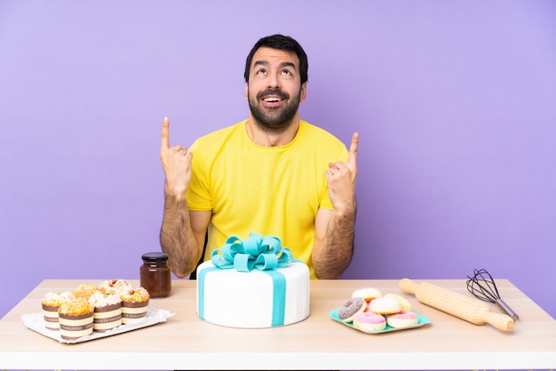 Mann in einem Tisch mit einem großen Kuchen überrascht und zeigt nach oben