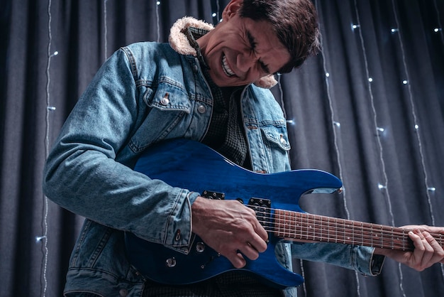 Mann in einer Jeansjacke spielt eine blaue E-Gitarre. Konzerte Konzept. Gemischte Medien