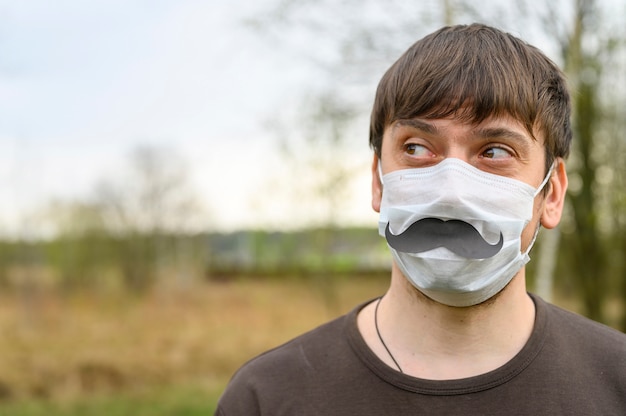 Mann in einer Schutzmaske und Papierschnurrbart im Wald