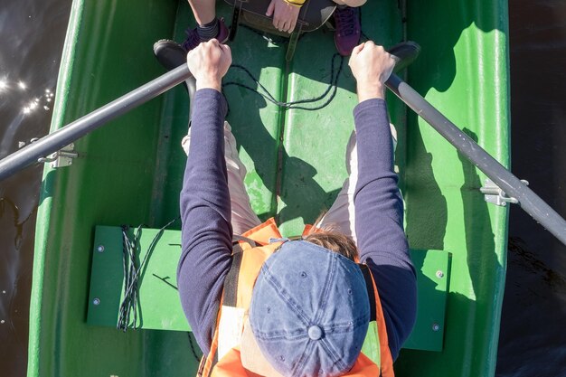 Mann in einer Schwimmweste rudert mit Rudern auf einem Boot und über den See