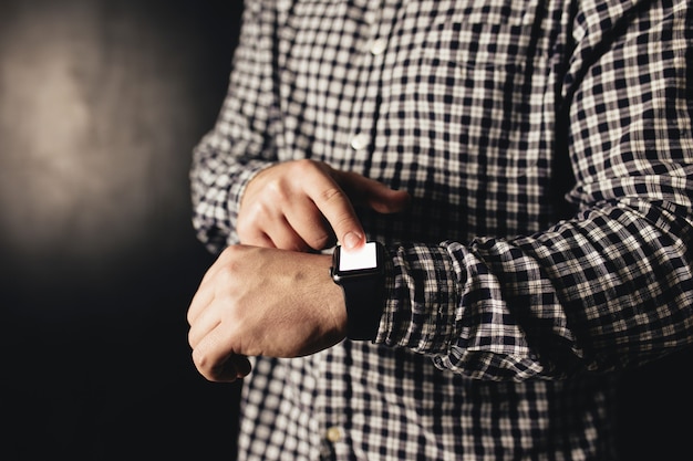 Foto mann in freizeitkleidung klickt auf handuhren, armband, schwarzen unscharfen hintergrund. hochwertiges foto