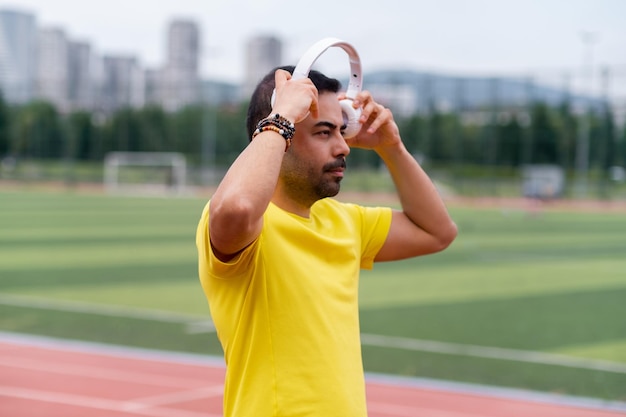 Mann in Gelb trägt drahtlose Kopfhörer, um mit inspirierender Musik im Sportstadion zu trainieren