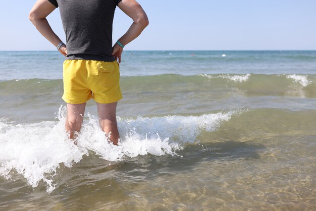 Mann in gelben Shorts steht im Meerwasser und schaut in die Ferne