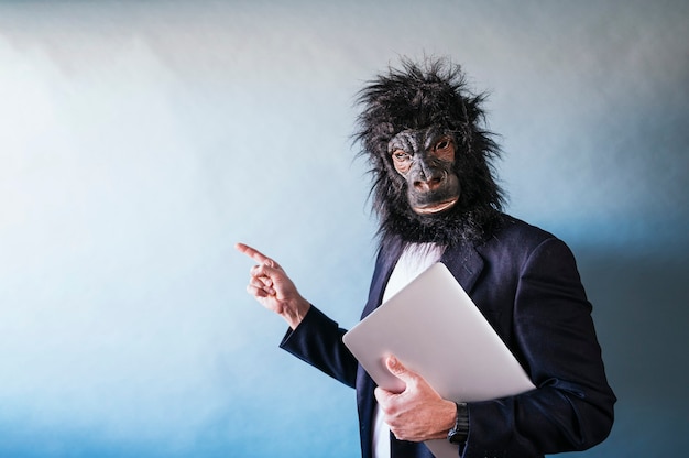 Mann in Gorillamaske mit Laptop unter dem Arm und mit dem Finger seitlich zeigend