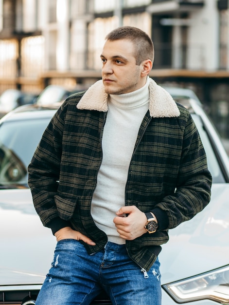 Mann in grüner karierter Jacke mit weißem Luxusauto