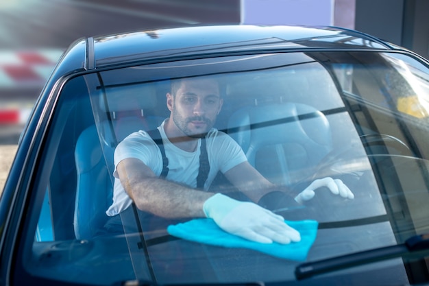 Mann in Handschuhen, der die Oberfläche im Auto abwischt