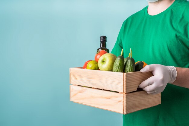 Mann in Handschuhen, die eine hölzerne Kiste voller Gemüse halten