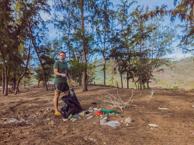 Mann in Handschuhen nimmt Plastik auf, das Meer und Wald verschmutzt Problem des verschütteten Müllmülls auf dem Strandsand, der durch eine vom Menschen verursachte Verschmutzungskampagne verursacht wird, um Freiwillige im Konzept zu reinigen