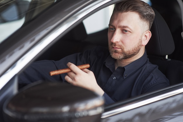 Mann in offizieller kleidung, der sein neues auto im autosalon versucht