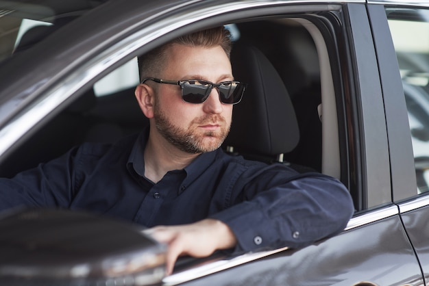 Mann in offizieller Kleidung, der sein neues Auto im Autosalon versucht