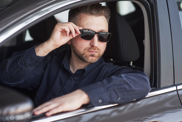 Mann in offizieller Kleidung, der sein neues Auto im Autosalon versucht