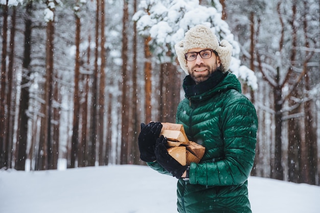 Mann in Pelzmütze mit Ohrenklappen, die einen Stapel Brennholz halten