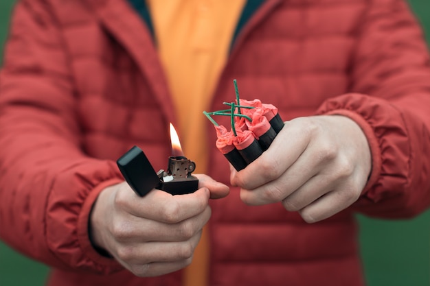 Mann in Red Jacked, der mehrere Feuerwerkskörper in seiner Hand mit Benzinfeuerzeug beleuchtet.