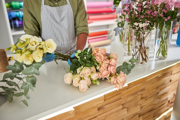 Mann in Schürze macht Blumenstrauß aus blühenden Rosen im Shop rose