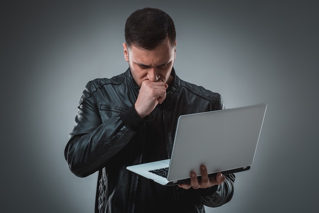 Mann in schwarzer Jacke mit Blick auf Laptop, halbe Drehung. Geöffneten Laptop halten und arbeiten. Emotion.