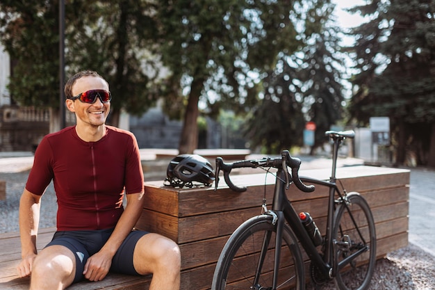 Mann in Sportkleidung sitzt neben dem Fahrrad und lächelt