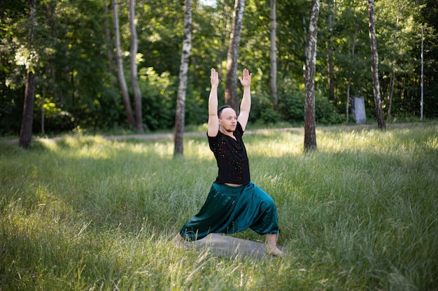 Mann in Sportkleidung steht in einer Asana, die draußen Yoga auf grünem Gras praktiziert. Internationaler Yogatag