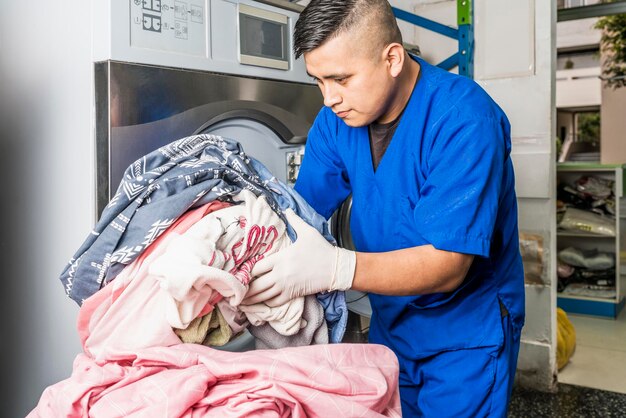 Mann in Uniform, der Kleidung in eine Industriewaschmaschine einführt