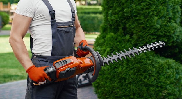 Mann in Uniform posiert im Garten mit elektrischem Trimmer