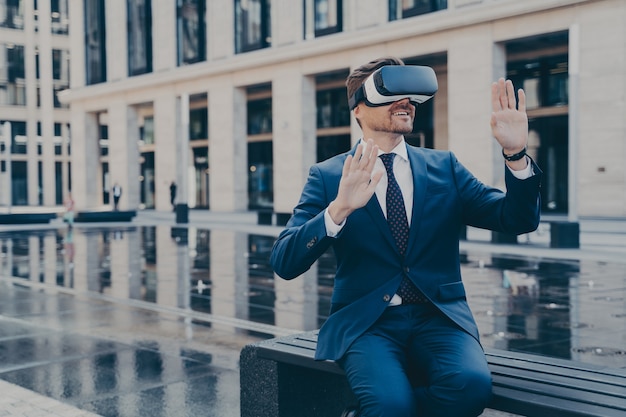 Mann in VR-Brille, der versucht, mit seinen Händen etwas in der virtuellen Realität zu erreichen, während er im Freien sitzt