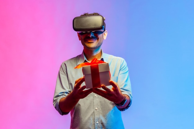 Mann in VR-Virtual-Reality-Brille, der eine verpackte Geschenkbox hält und freudig lächelt und ein Geschenk gibt