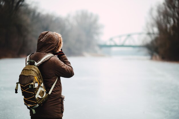 Mann in warmen Kleidern mit Rucksack steht auf einem Schneefeld