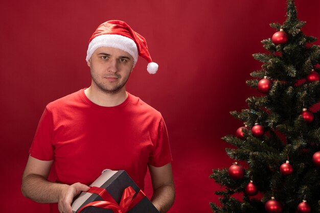 Mann in Weihnachtsmannmütze und rotem T-Shirt hält Geschenkbox mit Weihnachtsgeschenk