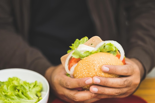 Mann isst Frühstück Hamburgerbrötchen gefüllt mit Gemüse und Fleisch und Tomaten Gesundes Frühstück Es hat gute Kohlenhydrate und Vitamine. Fast Food am Morgen vor der Arbeit