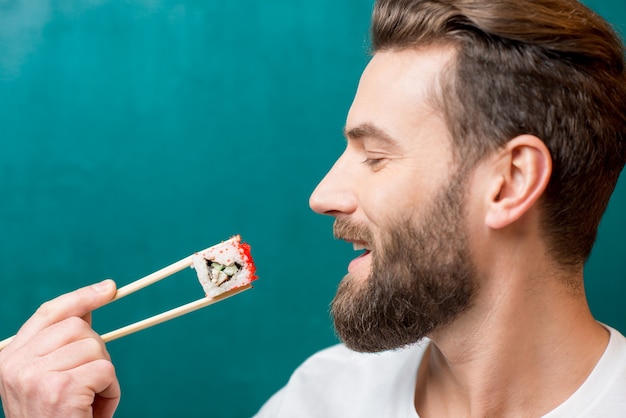 Foto mann isst sushi mit stäbchen auf grünem hintergrund