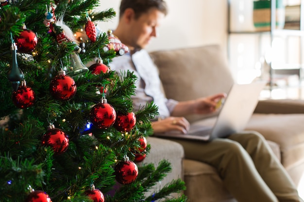 Mann kauft Weihnachtsgeschenke für das neue Jahr online mit Telefon-Laptop