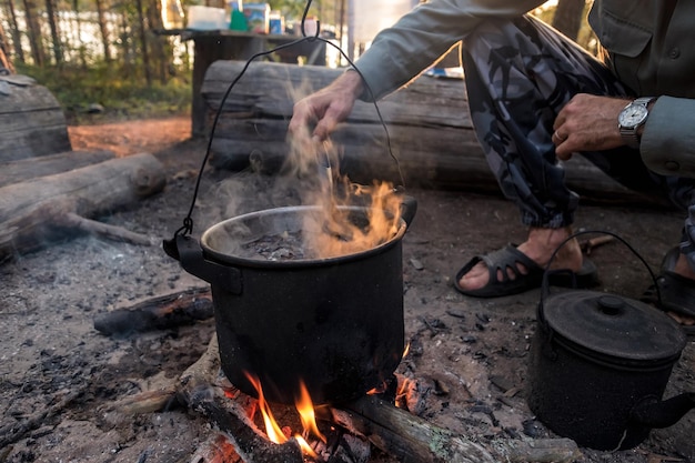 Mann kocht in Keglern über einem Feuer im Wald