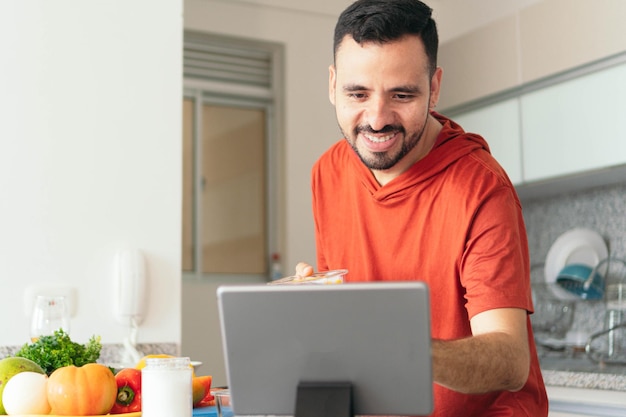 Mann kocht und benutzt sein Tablet in der Küche