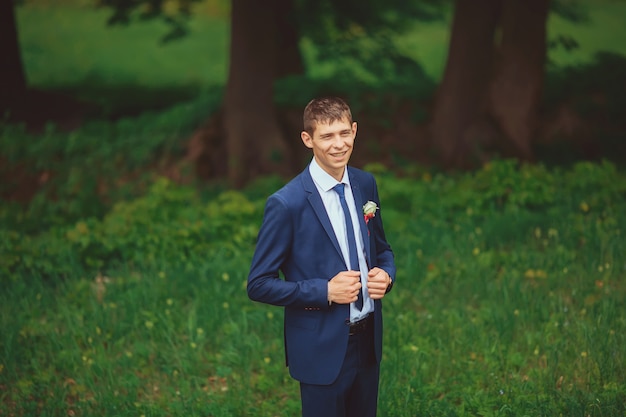 Mann lächelt. Porträt des gutaussehenden Mannes. Mann mit großem Lächeln gegen Naturhintergrund. Glücklicher Bräutigam. Groomsman. Porträt des Bräutigams im Park am Hochzeitstag