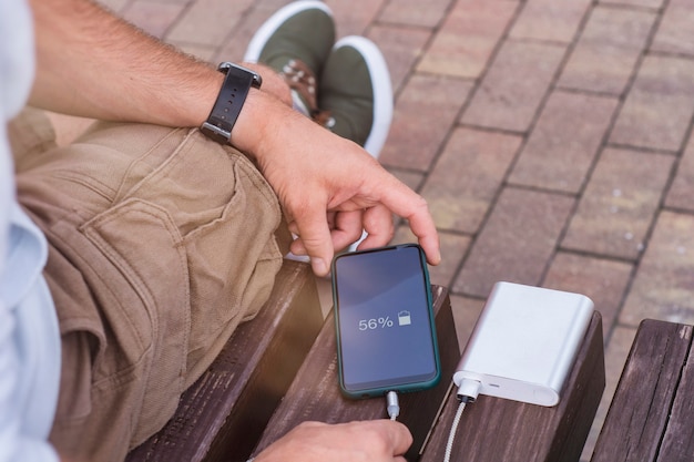 Mann lädt ein Smartphone mit einer Powerbank in der Hand. Tragbares Ladegerät zum Aufladen von Geräten.