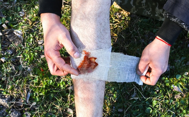 Mann legt Verband auf blutende Wunde. Verletztes Bein. Tourist in der Natur. Infektionsgefahr. Medizinische Behandlung. Wandertrauma.