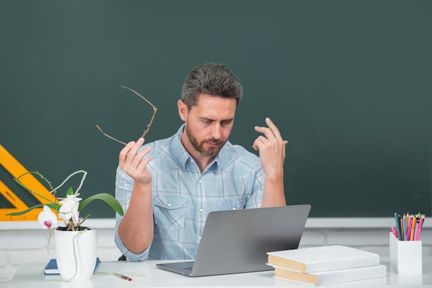 Mann-Lehrer-Porträt eines intelligenten jungen Tutors mit Brille mit Buch an der Tafel im Unterricht bei High Sc