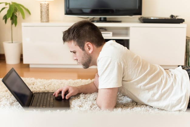 Mann liegt auf dem Boden und tippt auf Laptop