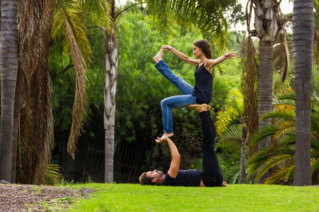 Mann liegt auf Gras als Basis für Frau als Flyer im Acroyoga-Kurs im Park Paar Yogis im Freien