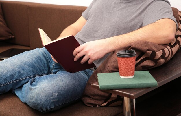 Mann liegt zu Hause auf braunem Sofa und liest Buch. Ansicht von oben