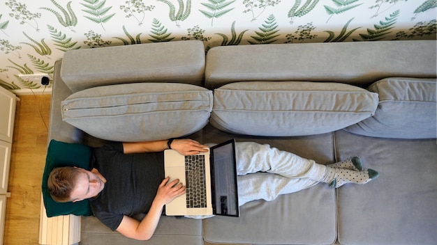 Mann liegt zu Hause auf dem Sofa mit einem Laptop auf seinem Schoß